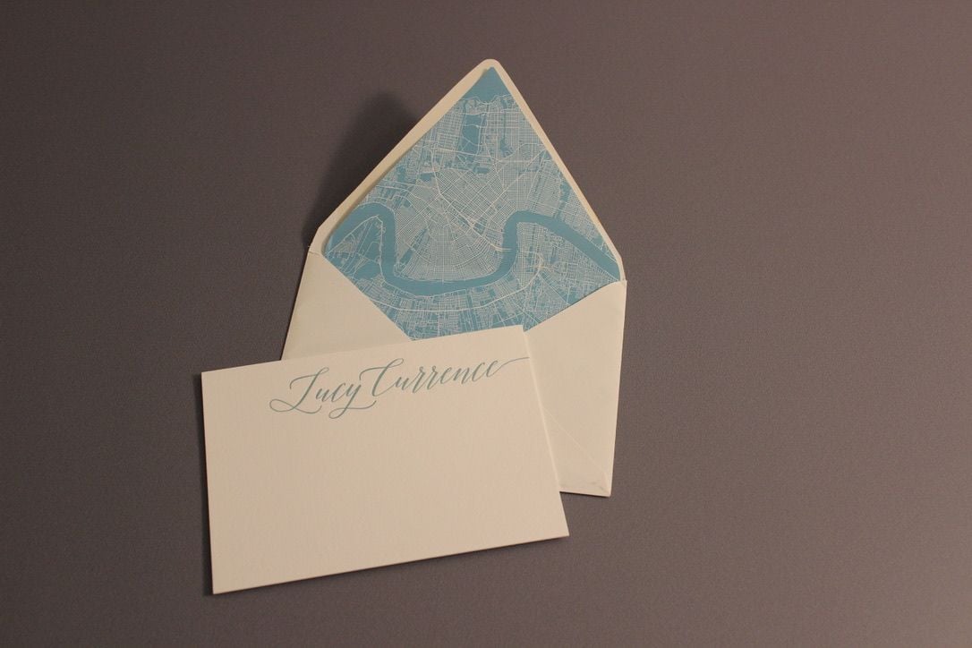 Cream envelope with a printed blue liner beside a card printed with an individual name