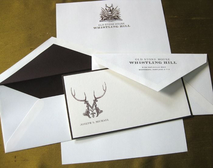 White stationery set with a stag crest, a printed card and a black lined envelope