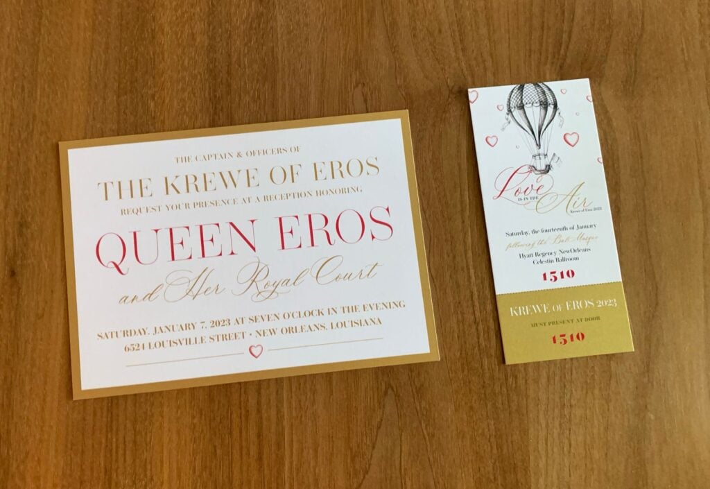 Printed Mardi Gras krewe invitation and matching ticket on a wooden table