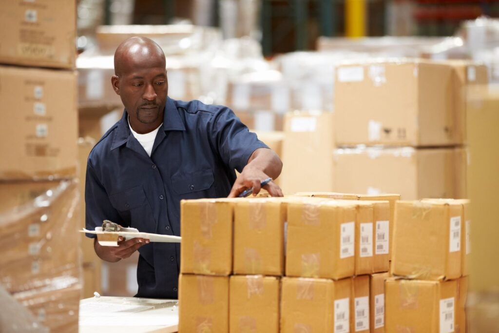 Warehouse team member checking cartons stacked on a pallet against a clipboard