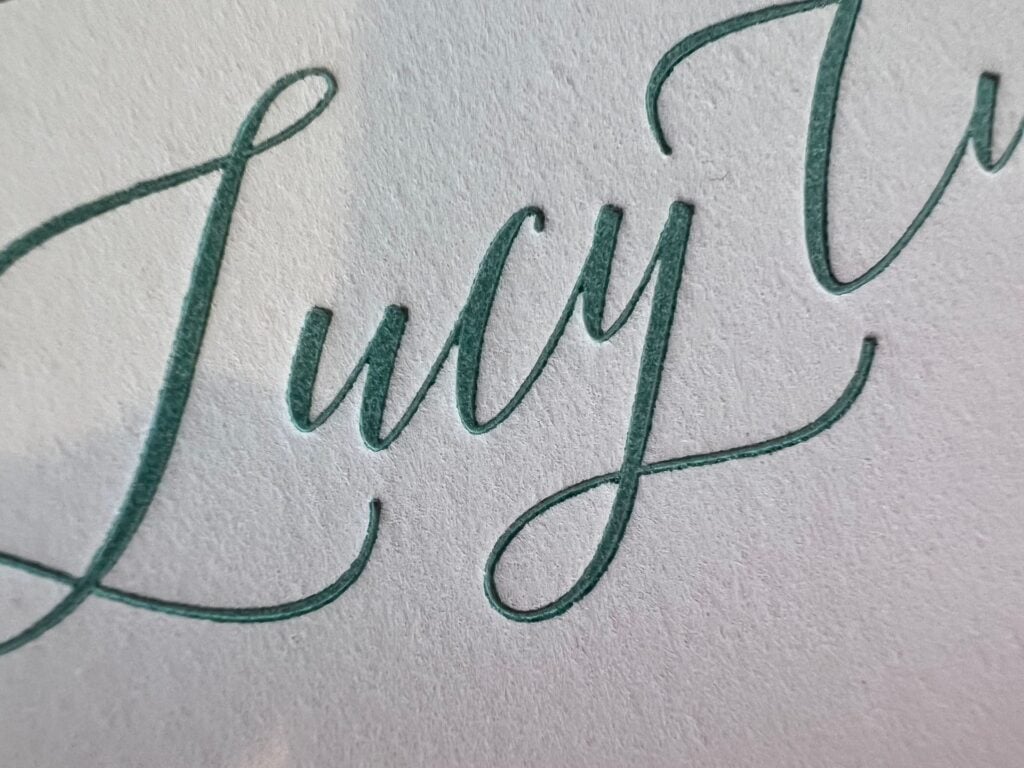 Close up of green calligraphy script letterpress printed into thick textured cotton stock