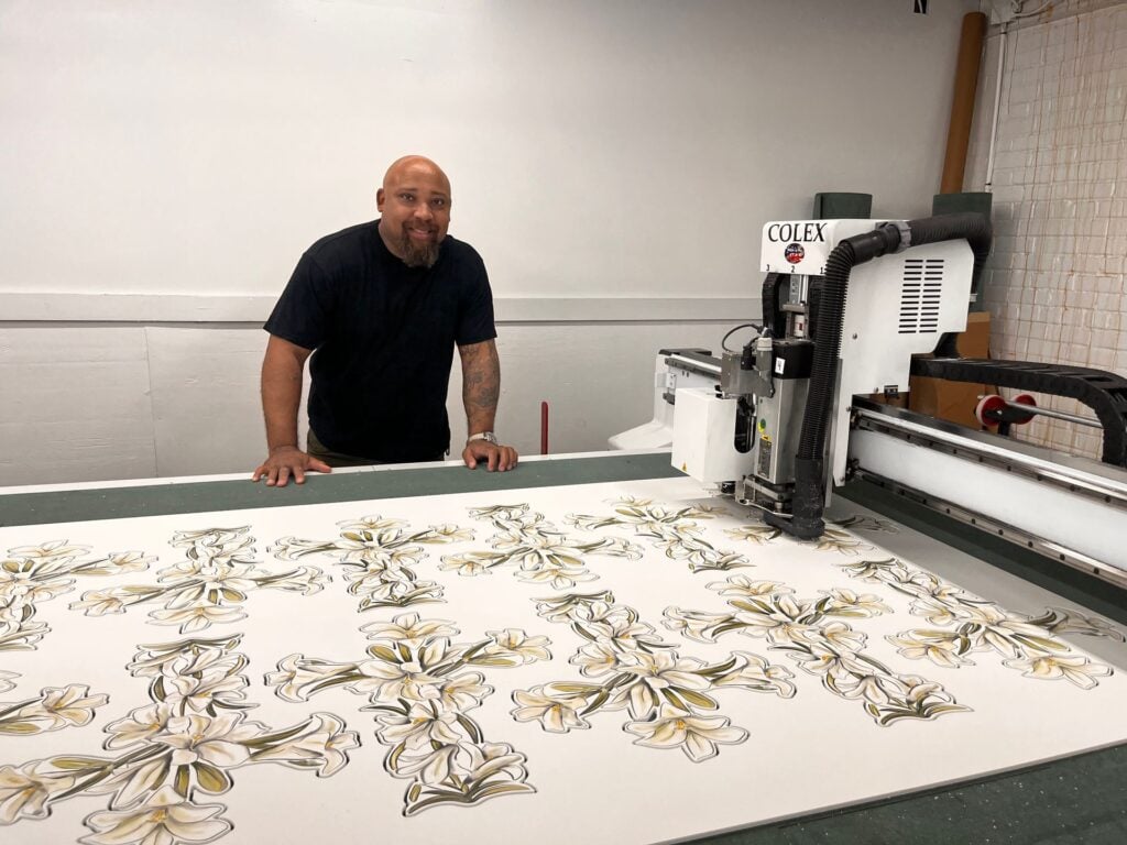 MPress team member at a flatbed cutting table with a large printed sheet of die cut shapes