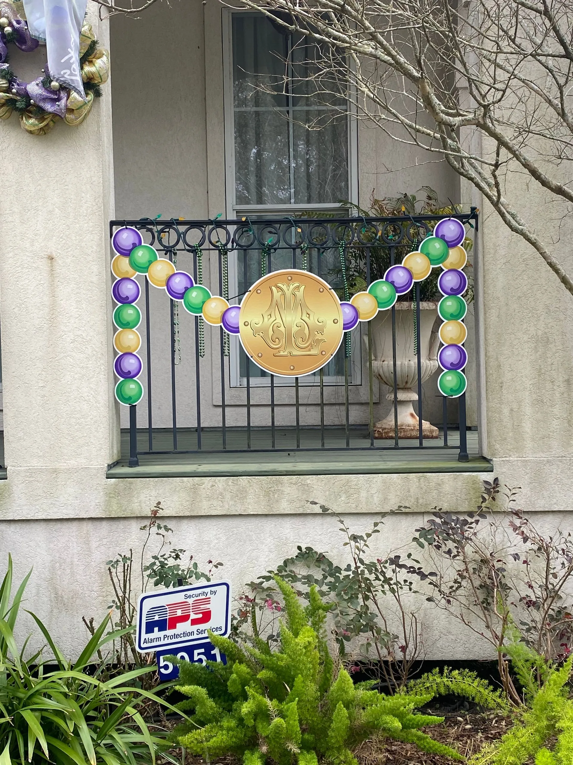 Die cut Mardi Gras decorations arching over a balcony railing above an MPress yard sign